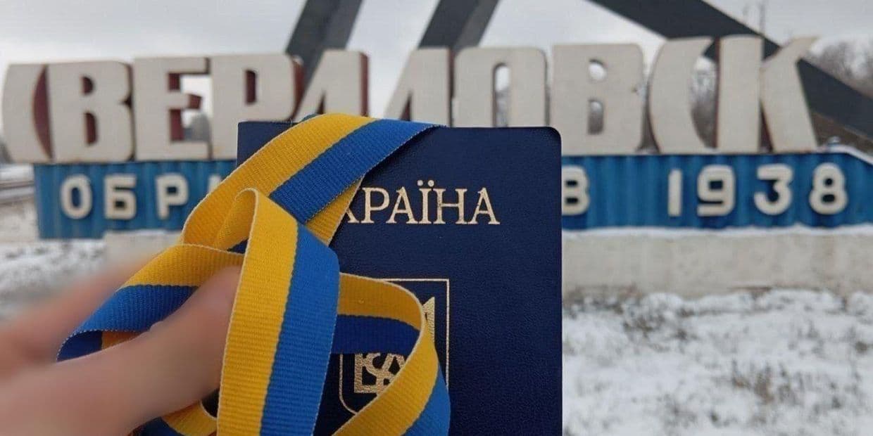 Український паспорт на фоні стели в окупованому Довжанську. Фото: Жовта Стрічка