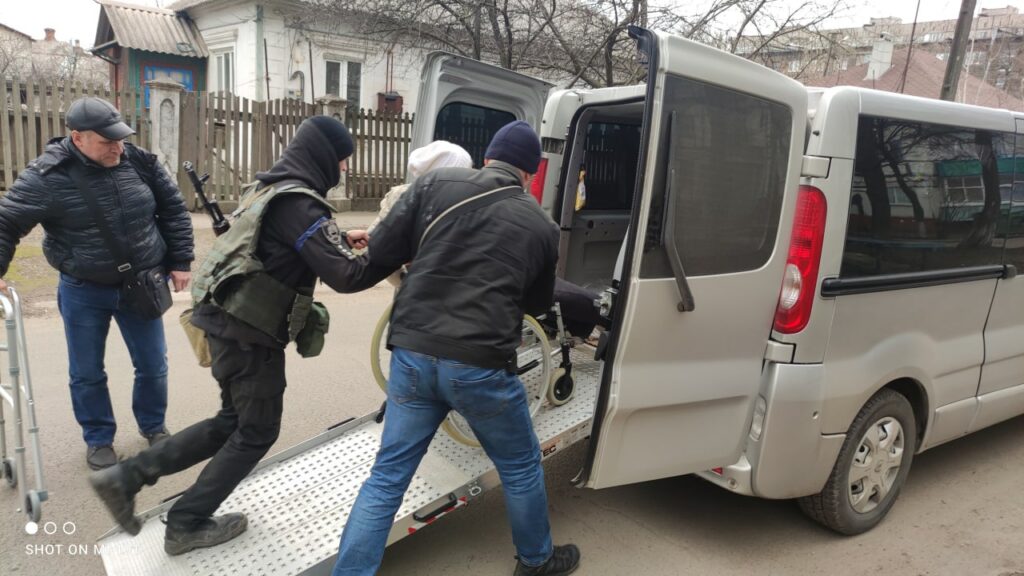 Катерина та її чоловік у супроводі поліції допомагають жінці на інвалідному візку евакуюватися в безпечний район до родичів